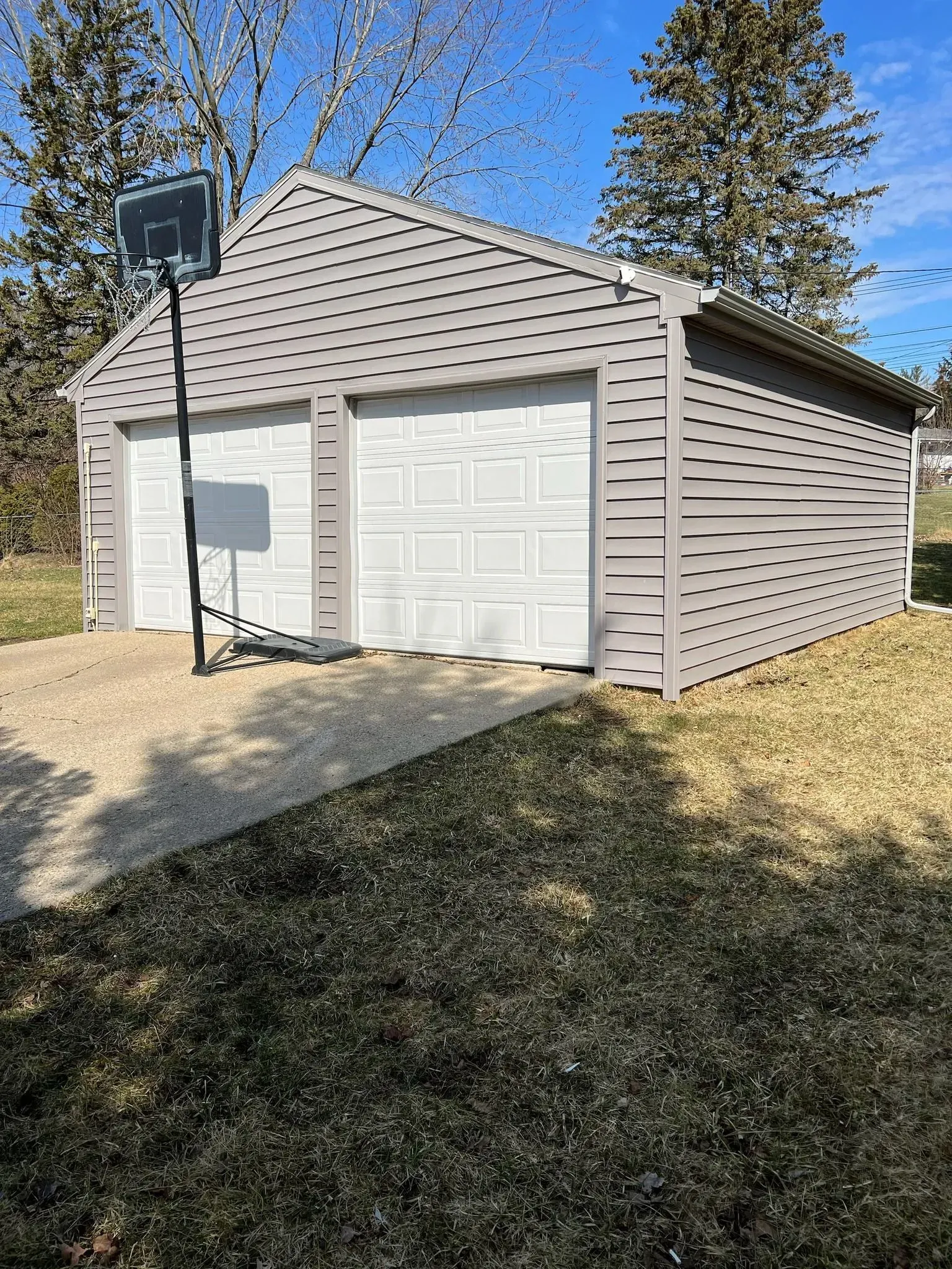 White garage with a basketball hoop beside a driveway under a clear blue sky.