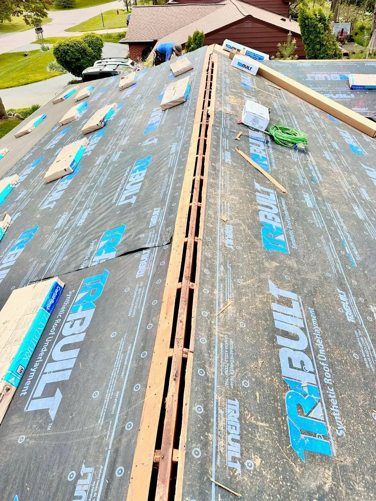 Roof under construction with black underlayment, blue tape, and a central ridge vent opening.