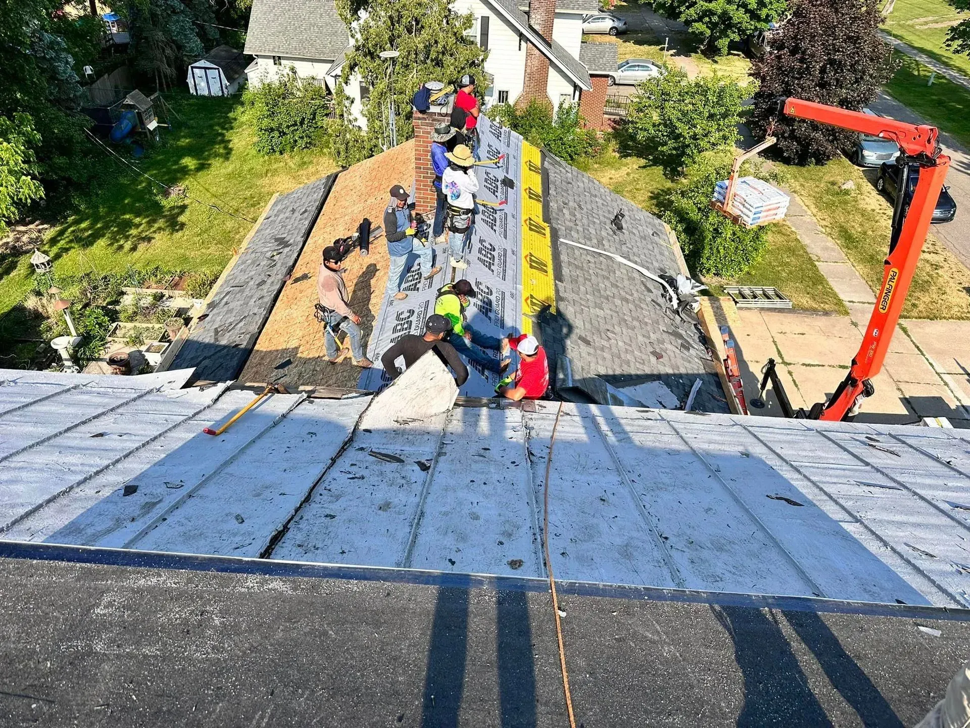 Roofers working on a steep roof with tools and materials, seen from above.