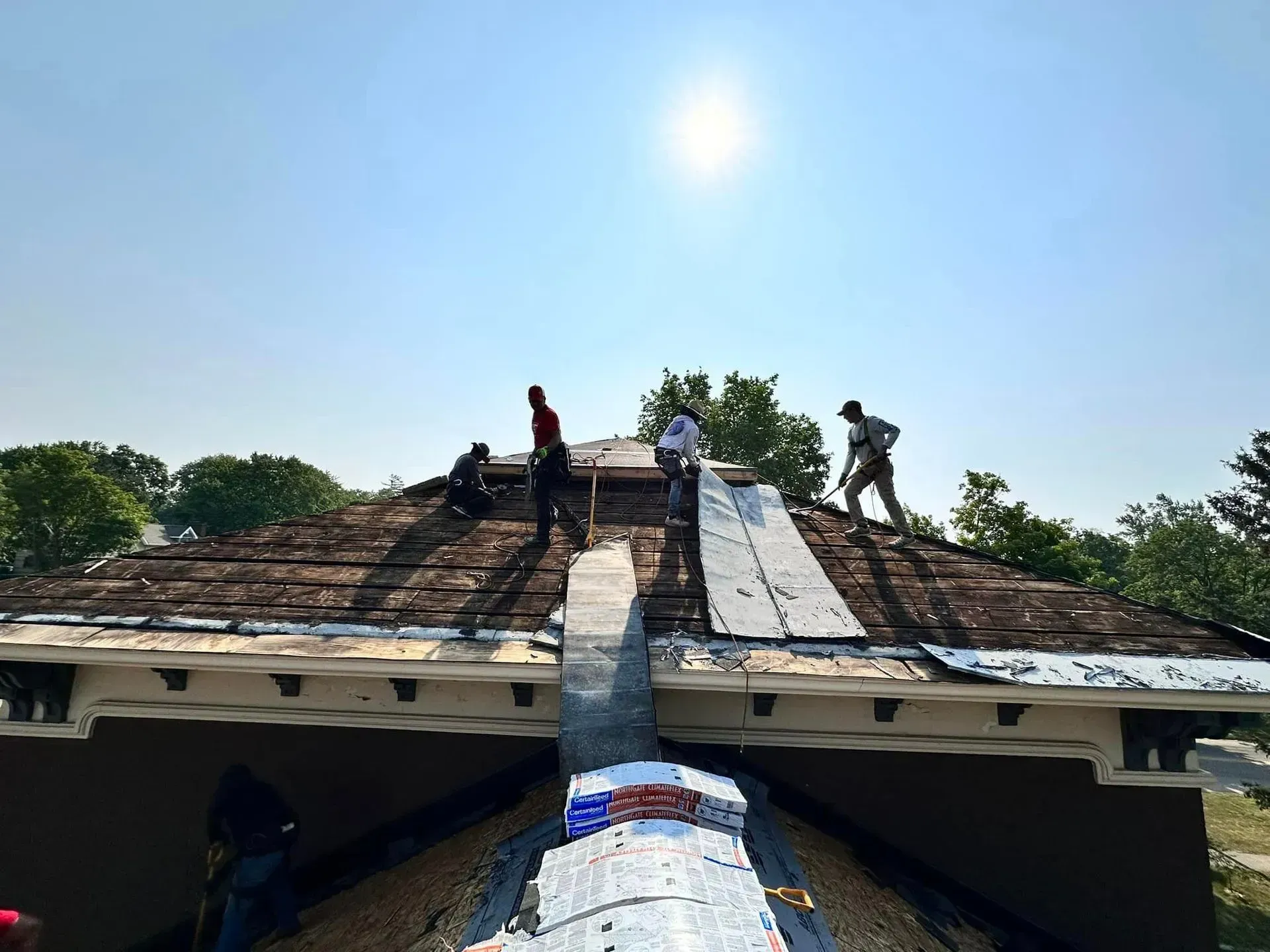 Workers repairing a roof with a long ladder under a bright blue sky