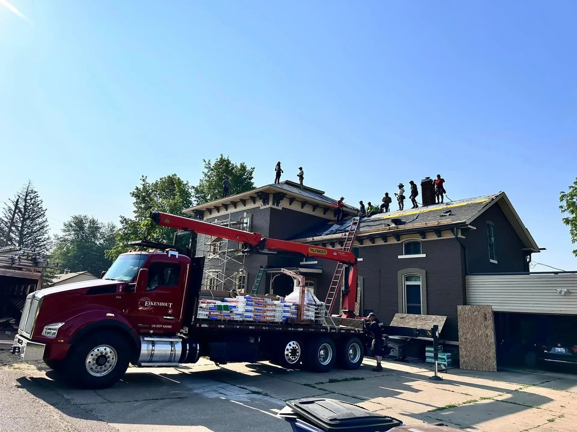 Red fire truck with ladder parked by a damaged house while roofers work on the roof