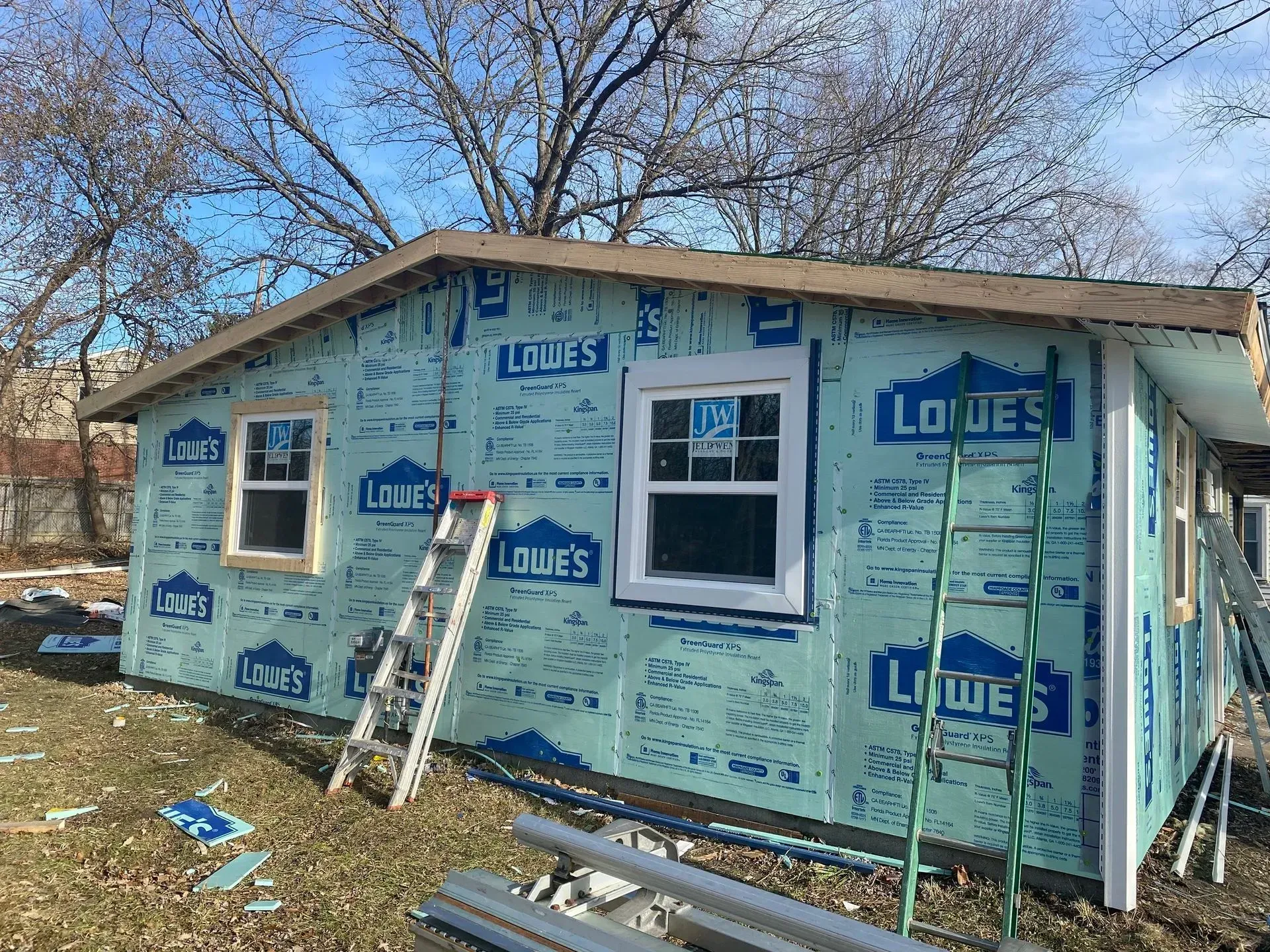 Partially renovated house wrapped in Lowe's building wrap with ladder leaning outside