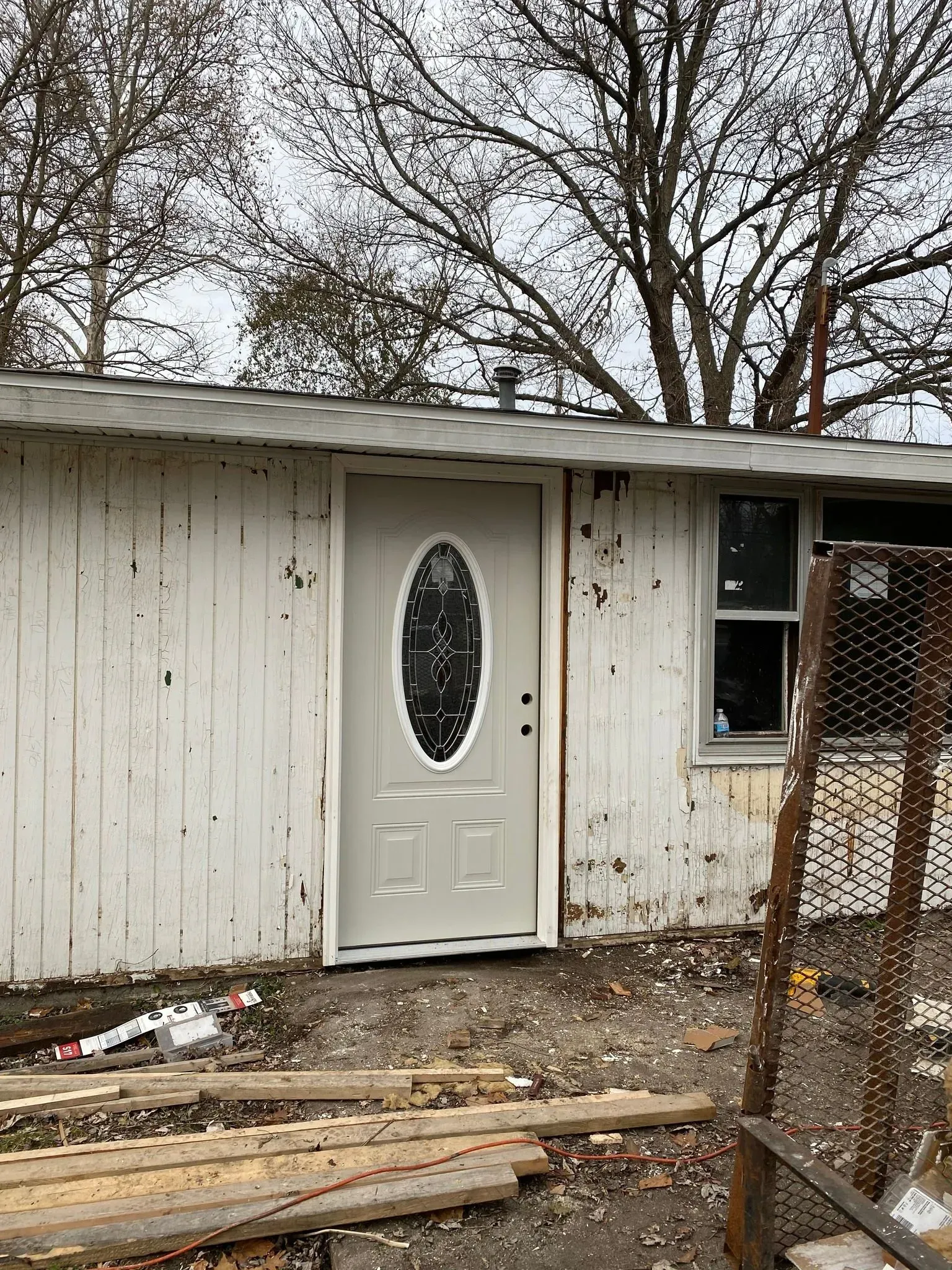 Small white house exterior with a white door, window, and debris in the yard.