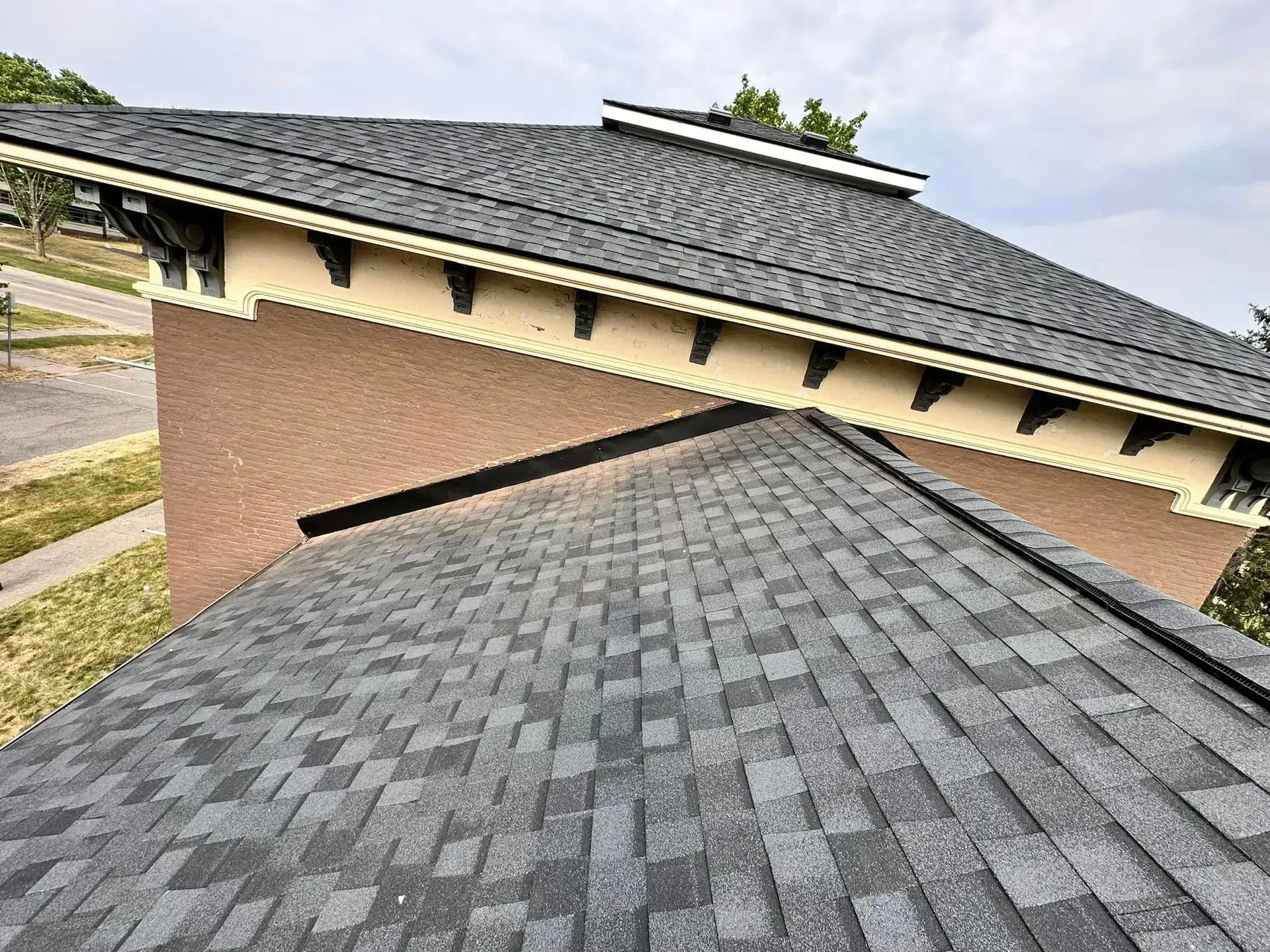 Close-up of gray shingled rooftops meeting at a brick building under a cloudy sky
