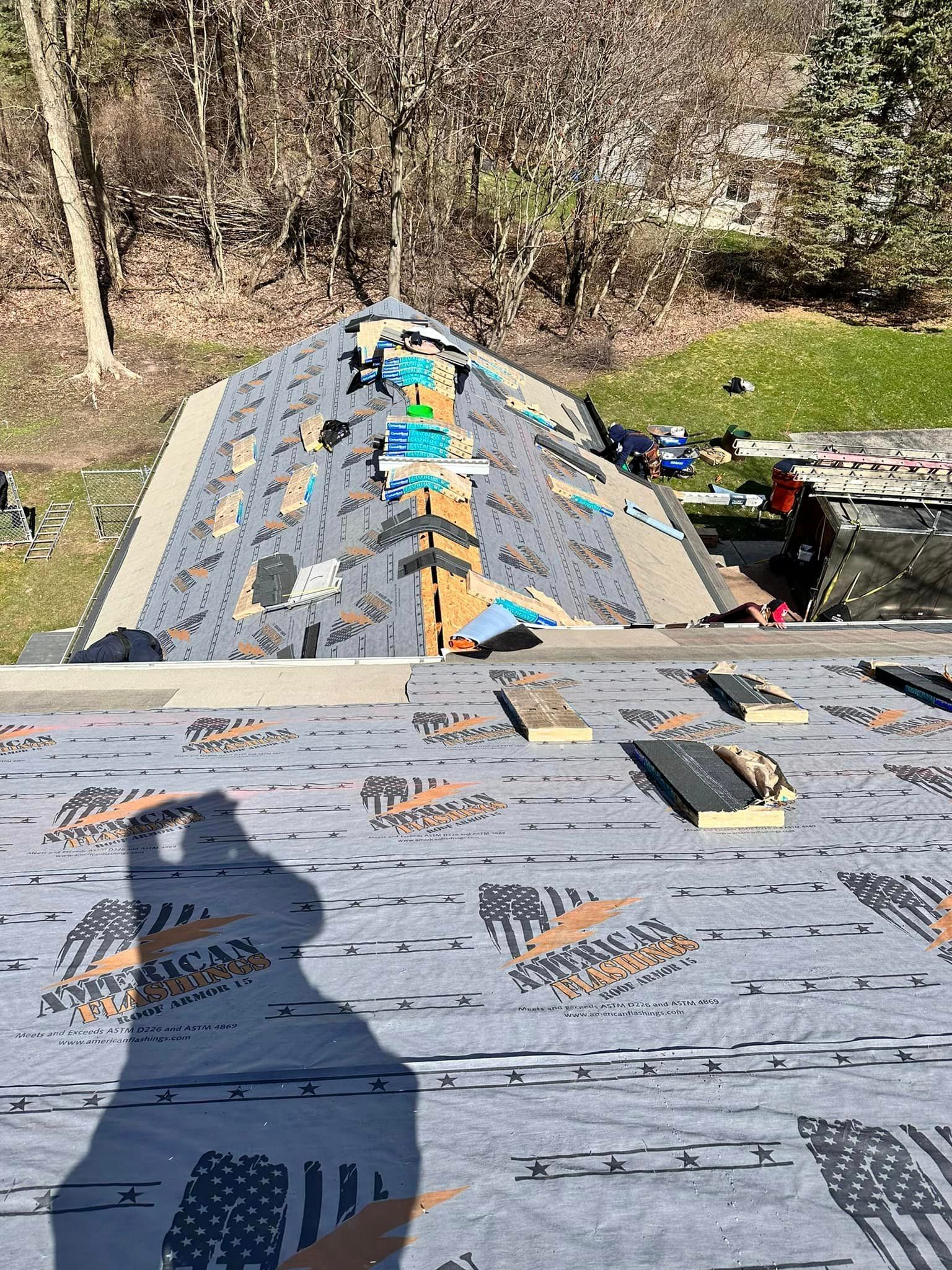 Roofing underlayment on a sloped roof with workers installing blue flashing strips