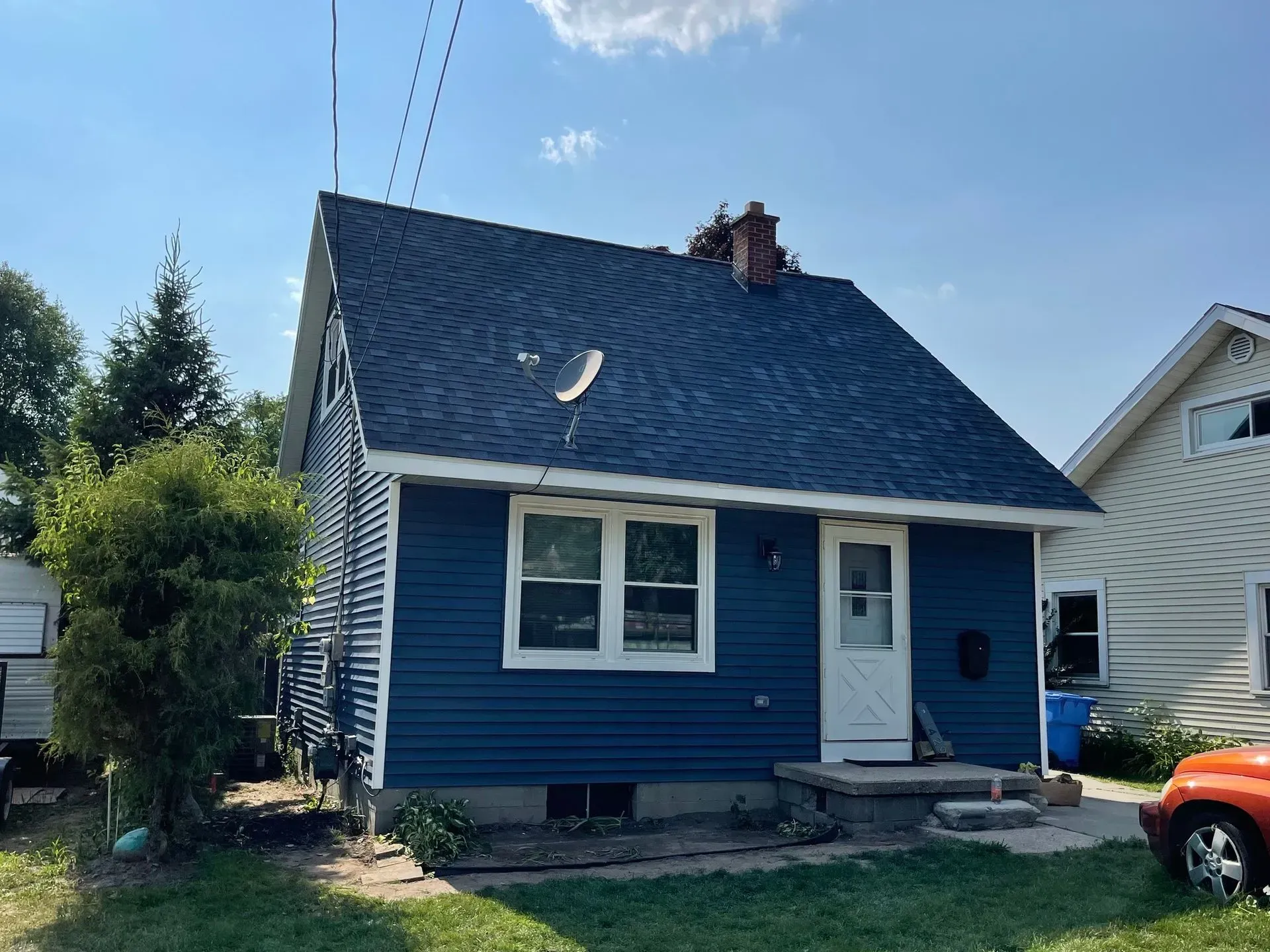Small blue house with white trim, steep shingled roof, and a front door under a bright sky.