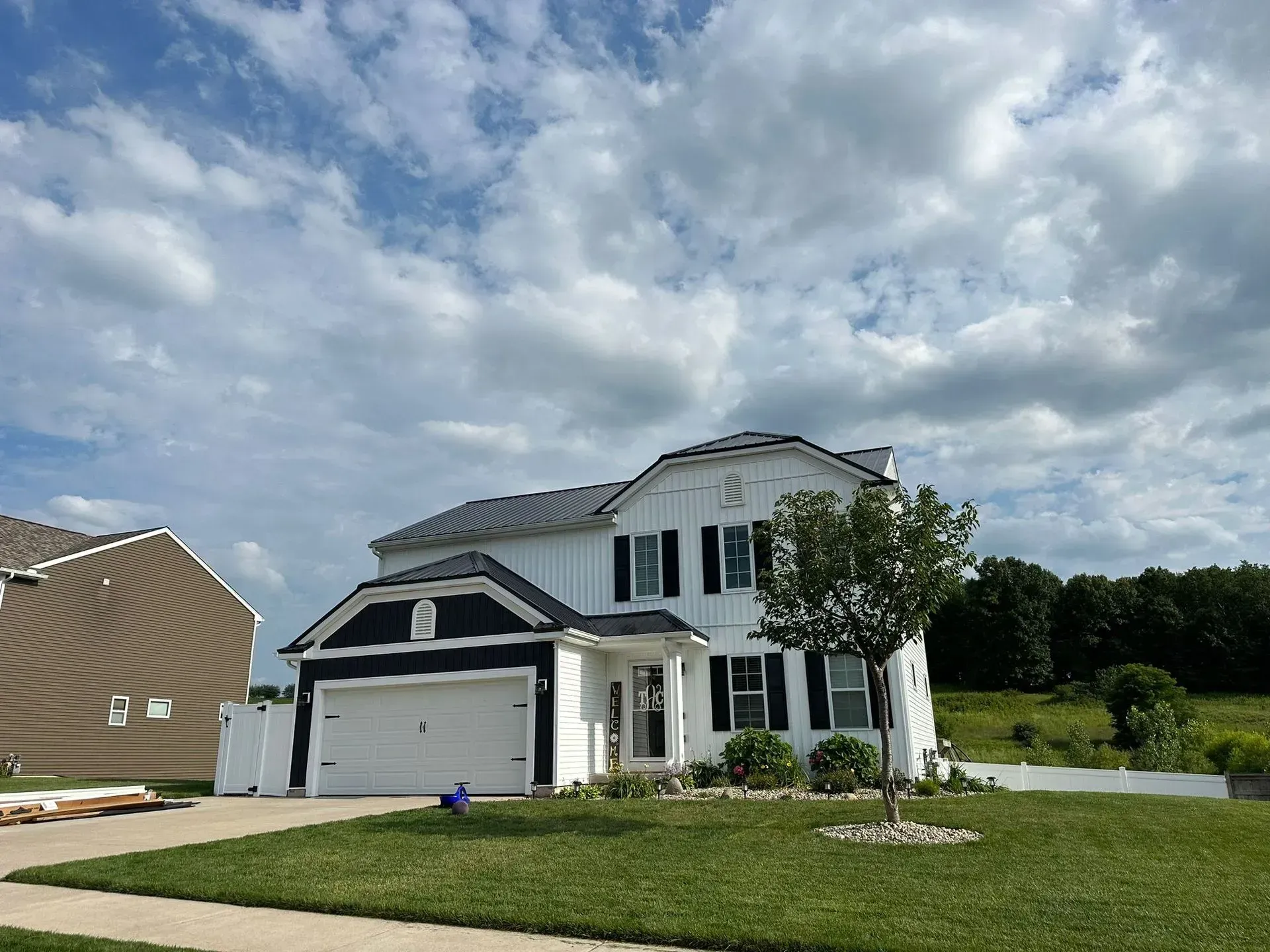 Two-story white house with dark shutters, a garage, and cloudy sky over a grassy suburban lot