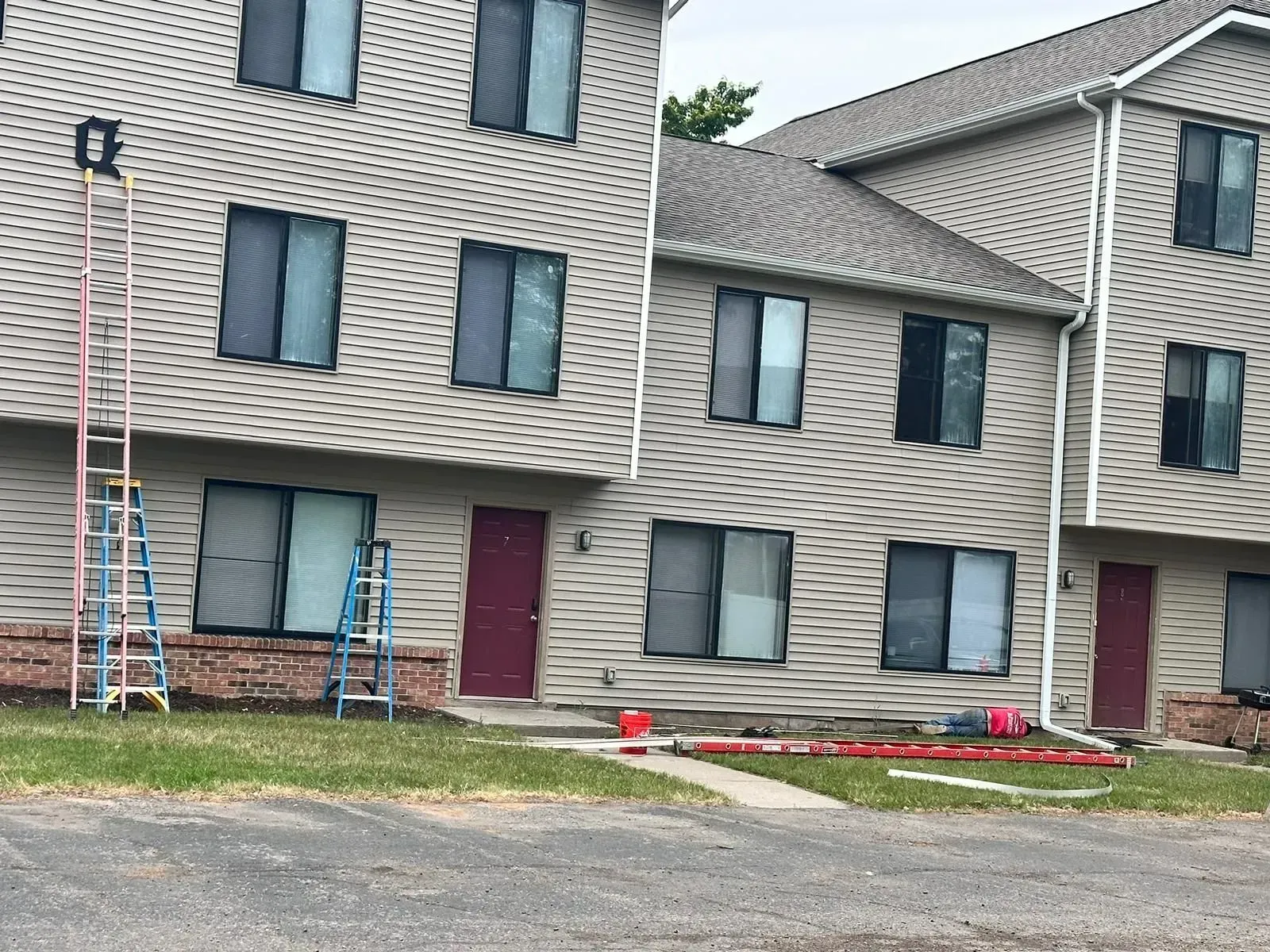 Apartment building with two red doors, dark windows, and ladders on the left side.
