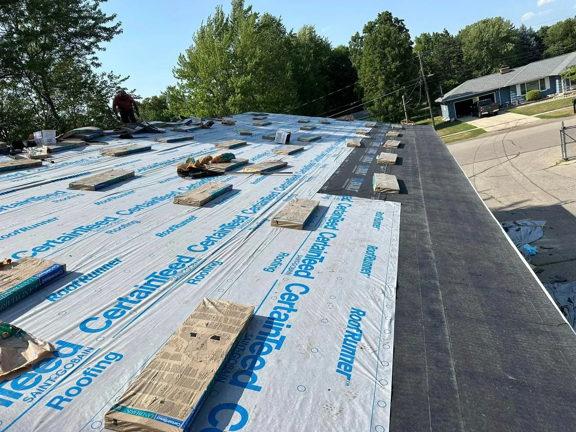 Roof under repair with blue waterproofing underlayment and workers on a steep roof slope