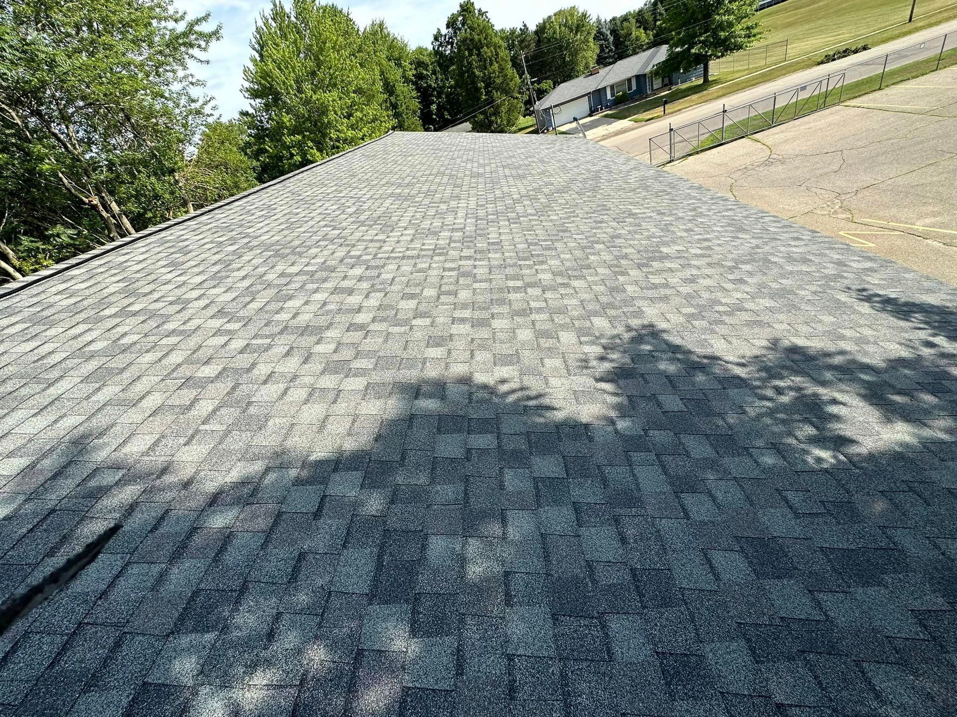 Dark gray shingled roof with trees and a sloped hillside in the background
