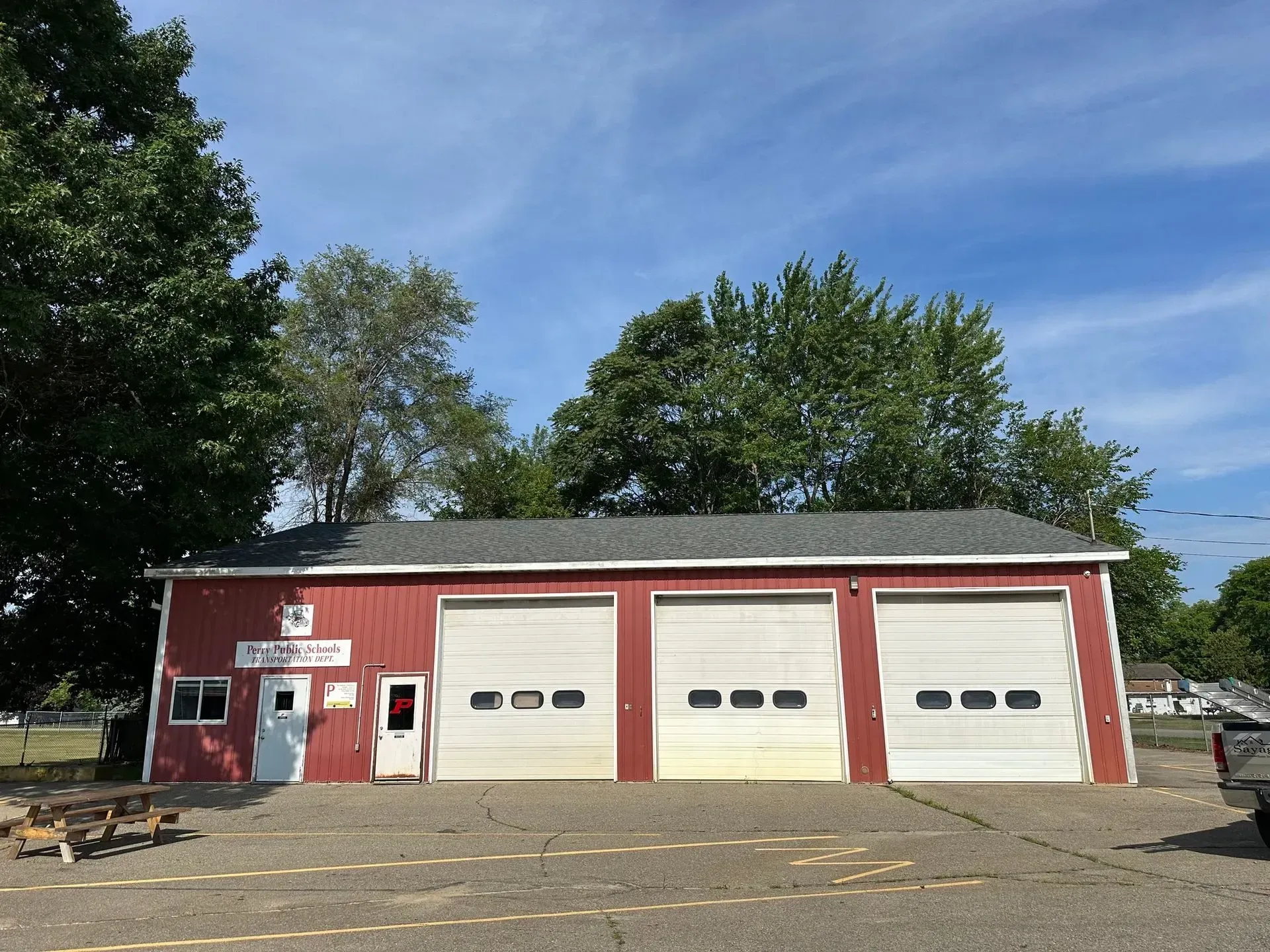 Red garage building with three white doors and trees under a blue sky