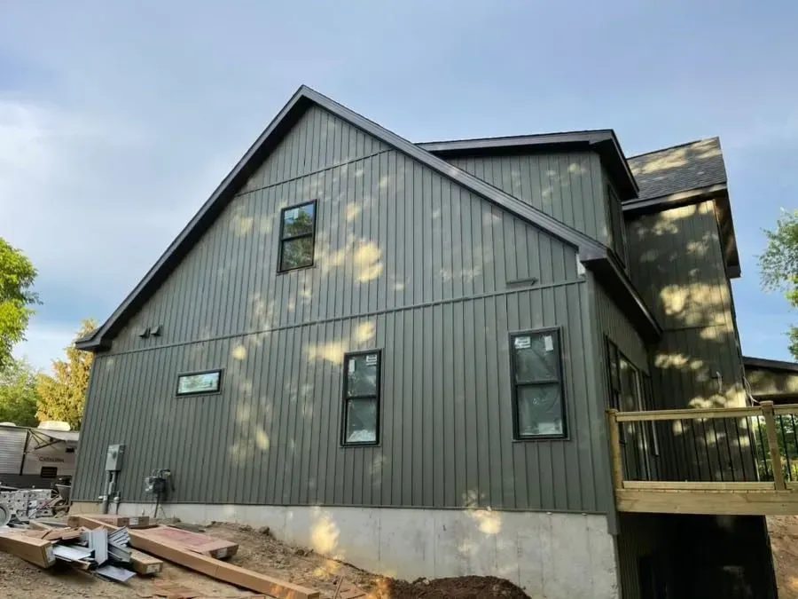 Gray modern house with steep roof, black-trimmed windows, and a small deck under construction