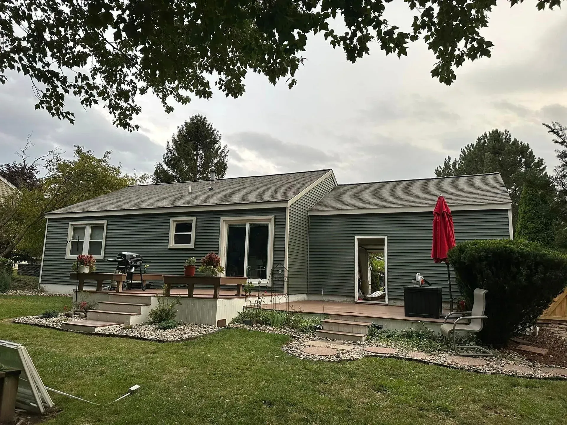 Single-story gray house with a front patio, lawn, and red patio umbrella under cloudy skies