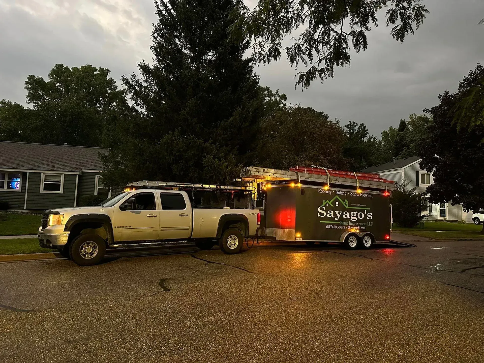 Pickup truck towing lit trailer on a wet residential street at dusk
