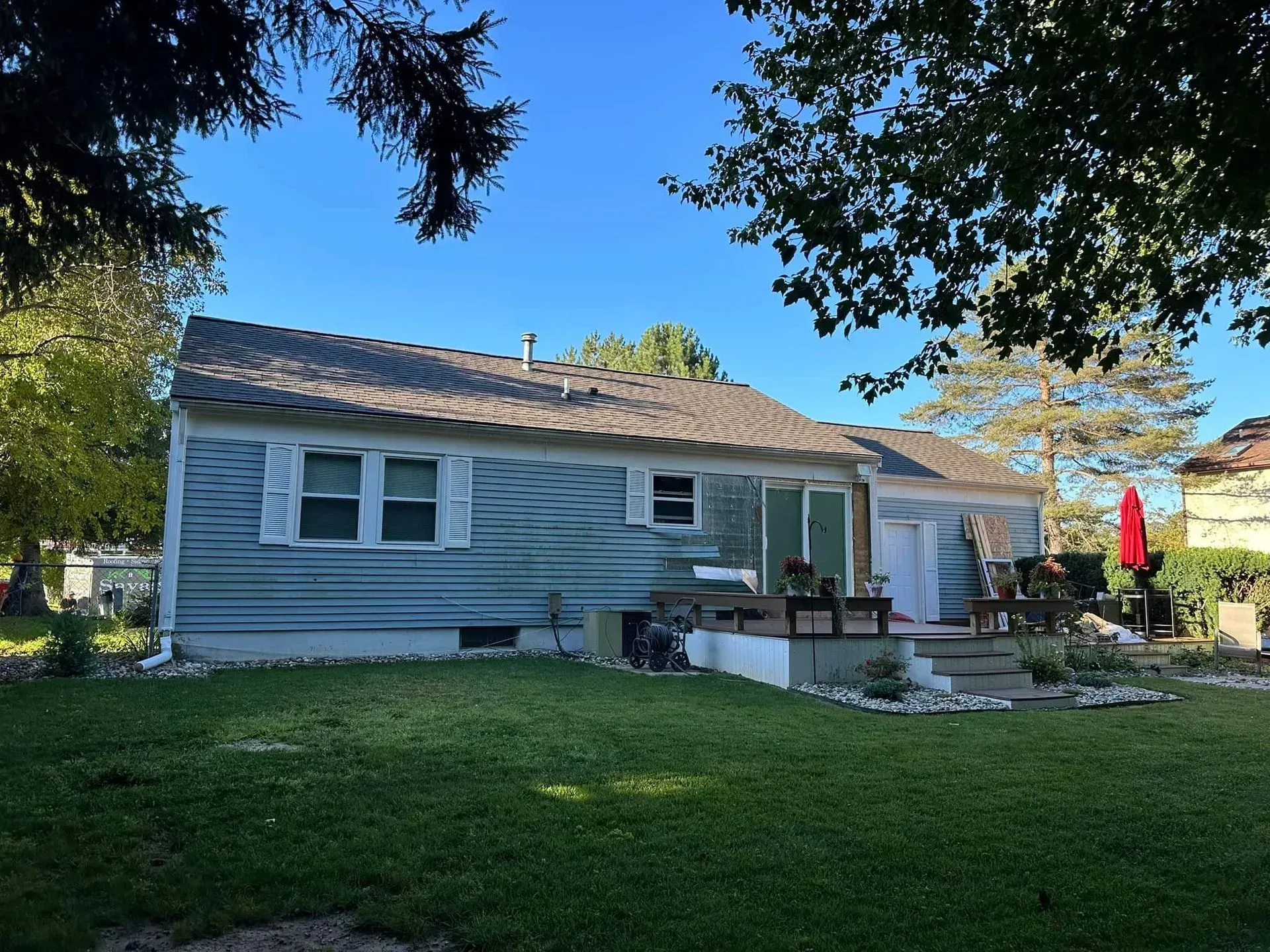 Single-story gray house with a front porch, lawn, and trees in the yard