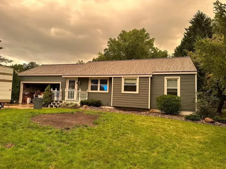 Single-story brown house with a garage, front yard, and cloudy evening sky