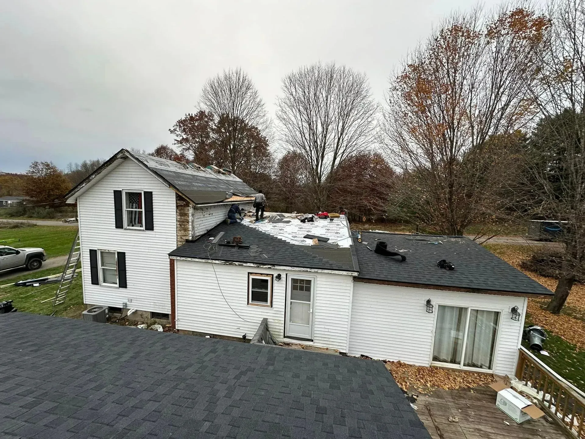 Aerial view of a damaged white house with a partially collapsed roof amid autumn trees