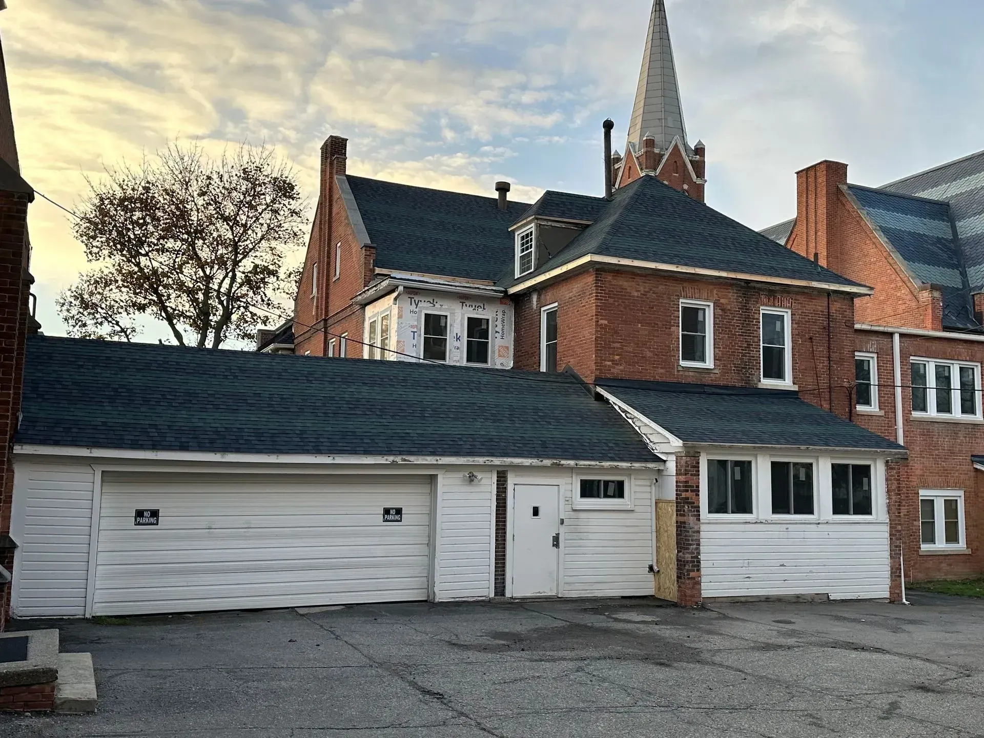 Brick house with attached white garage and church spire in the background at dusk