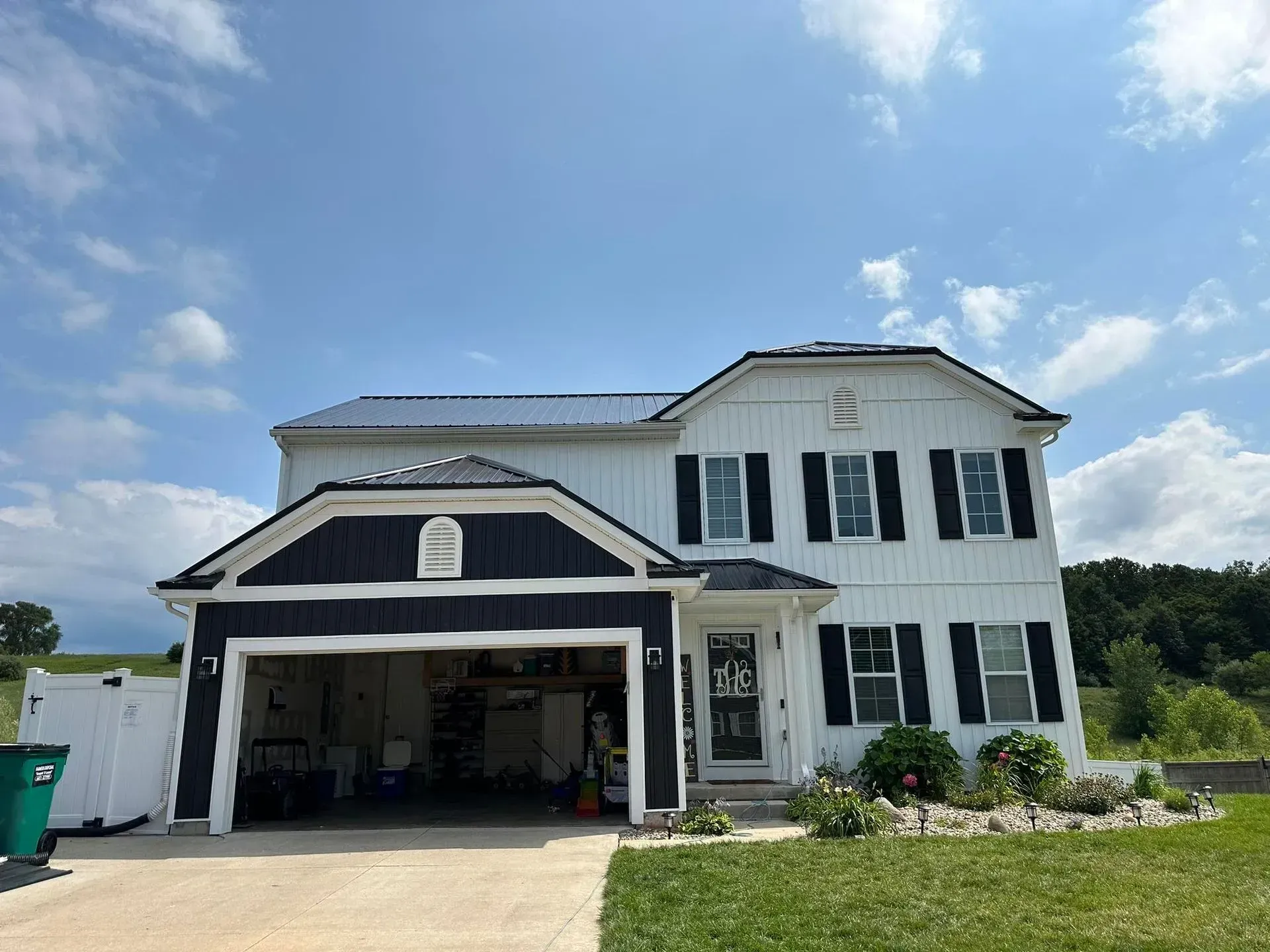 Two-story white house with navy trim and an open garage under a blue sky