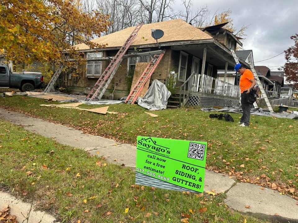 Damaged house with roof repair in progress, ladders and debris visible, bright green yard sign in front.