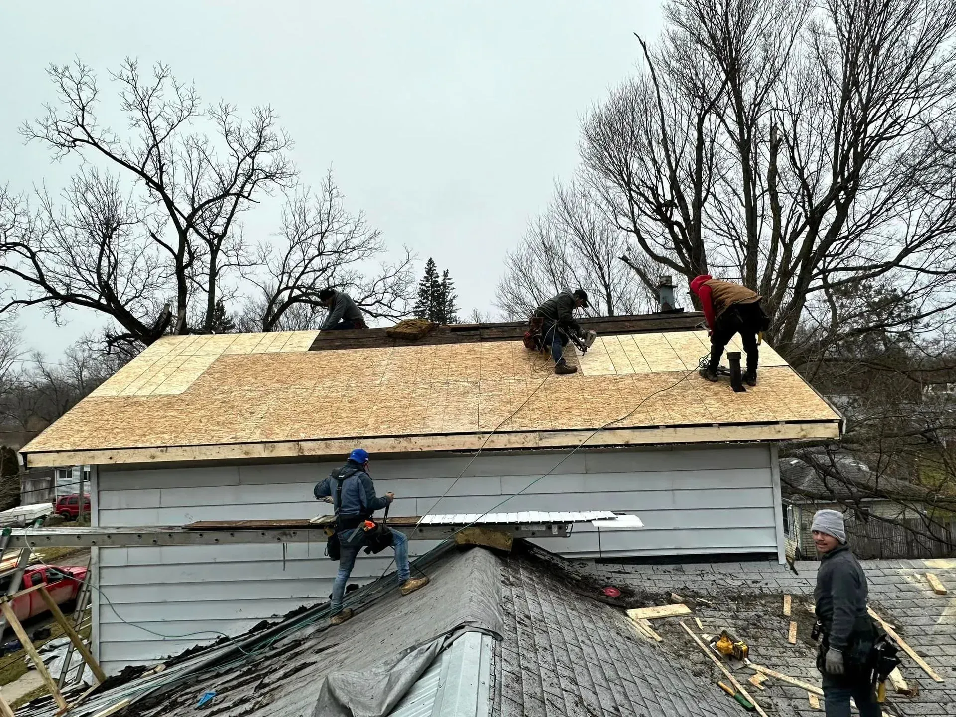 Workers repairing a damaged roof on a white building amid debris and bare trees