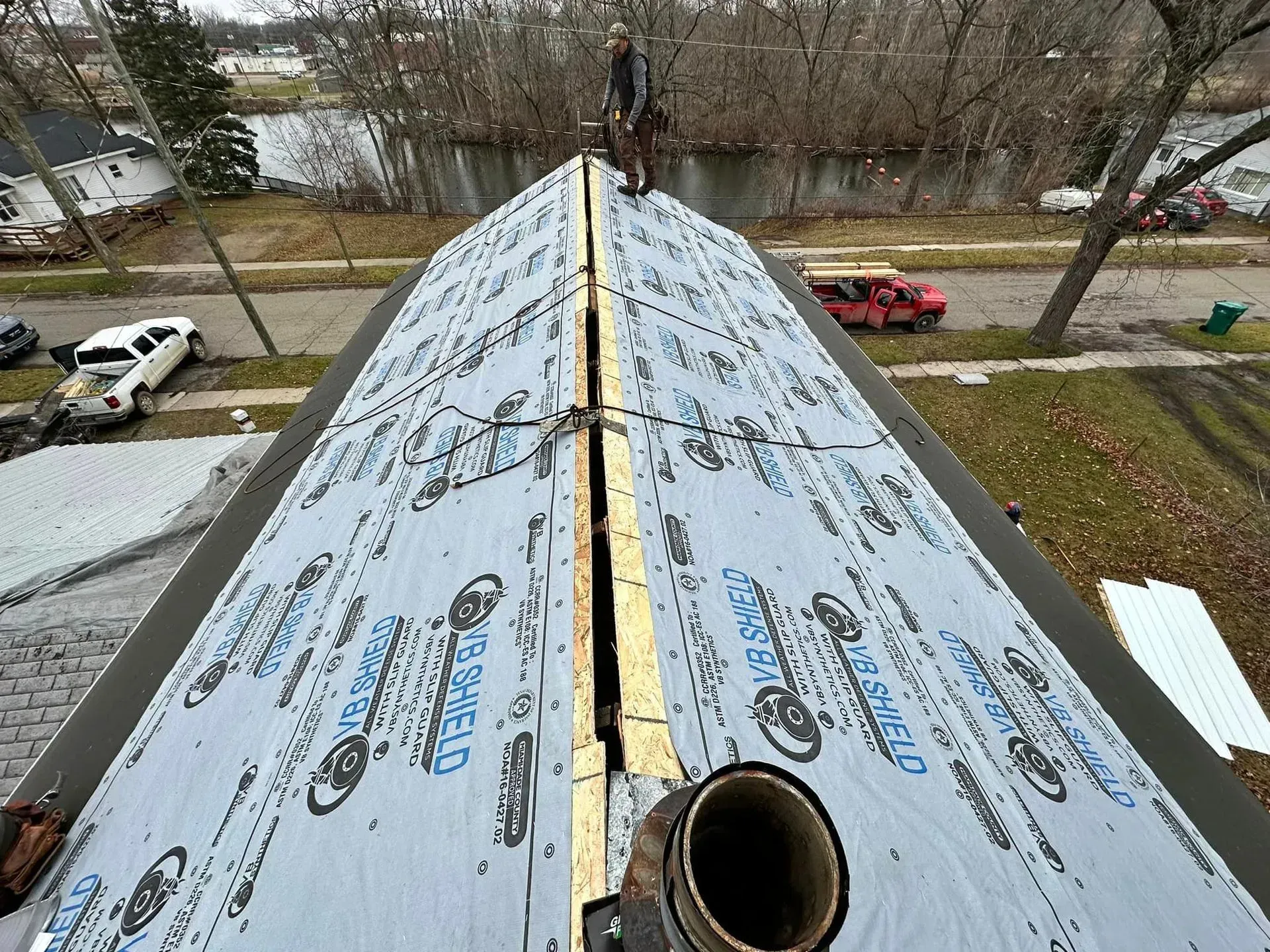 Roof under construction with gray underlayment and a ventilation pipe, viewed from the ridge.