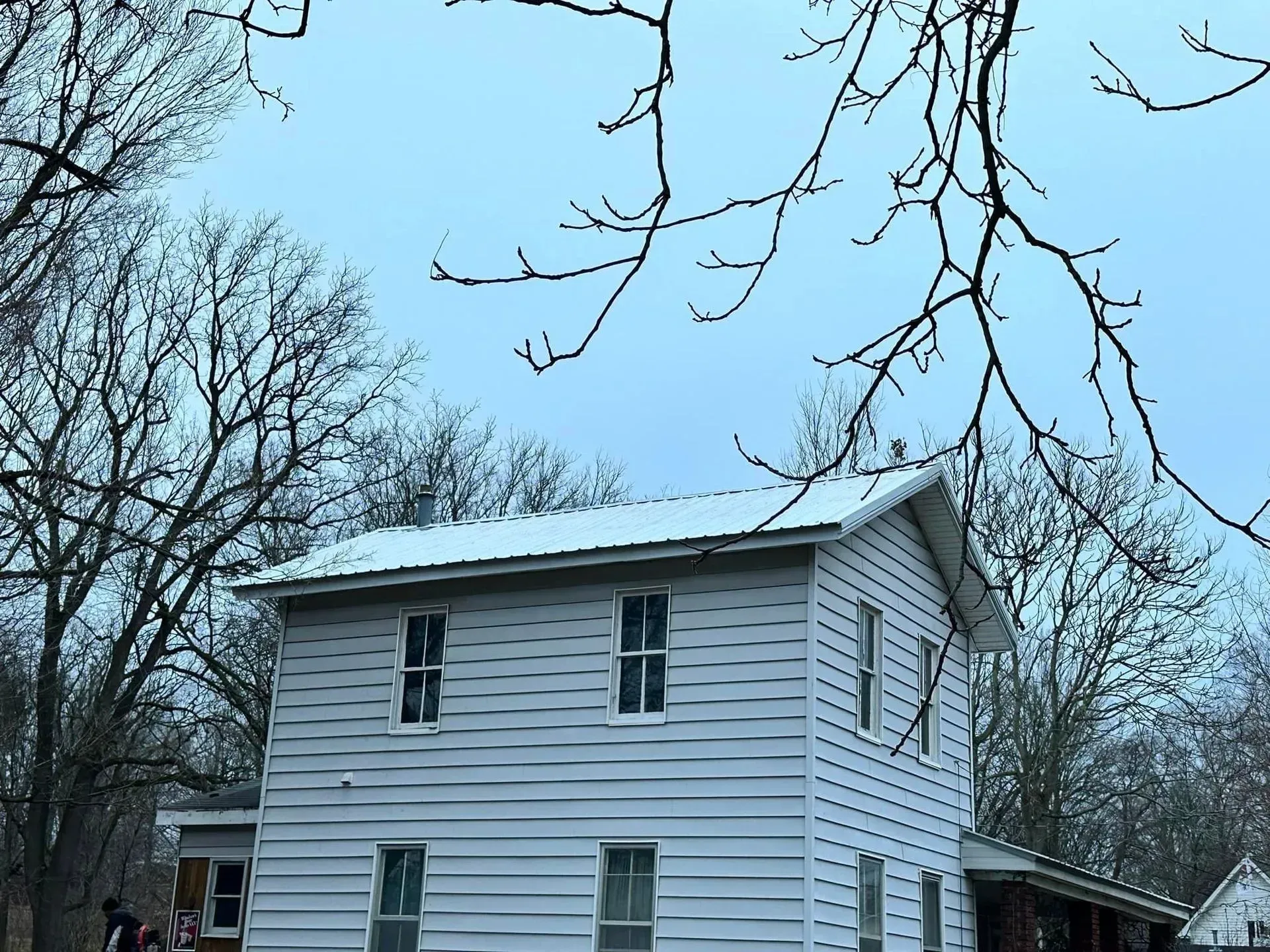 White two-story house with a sloped roof, surrounded by bare trees under a cloudy blue sky.