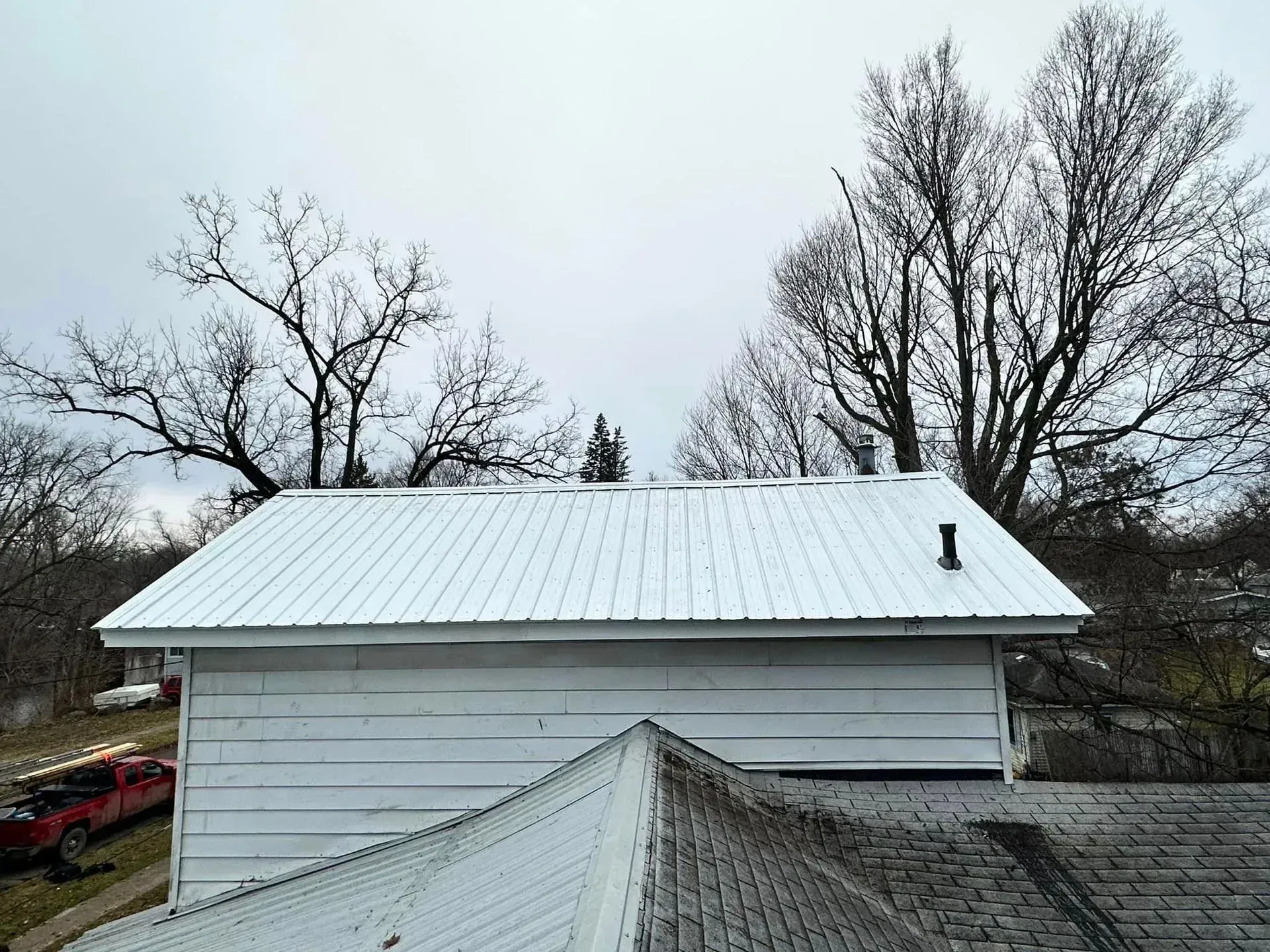 White metal roof on a house with bare trees under an overcast sky