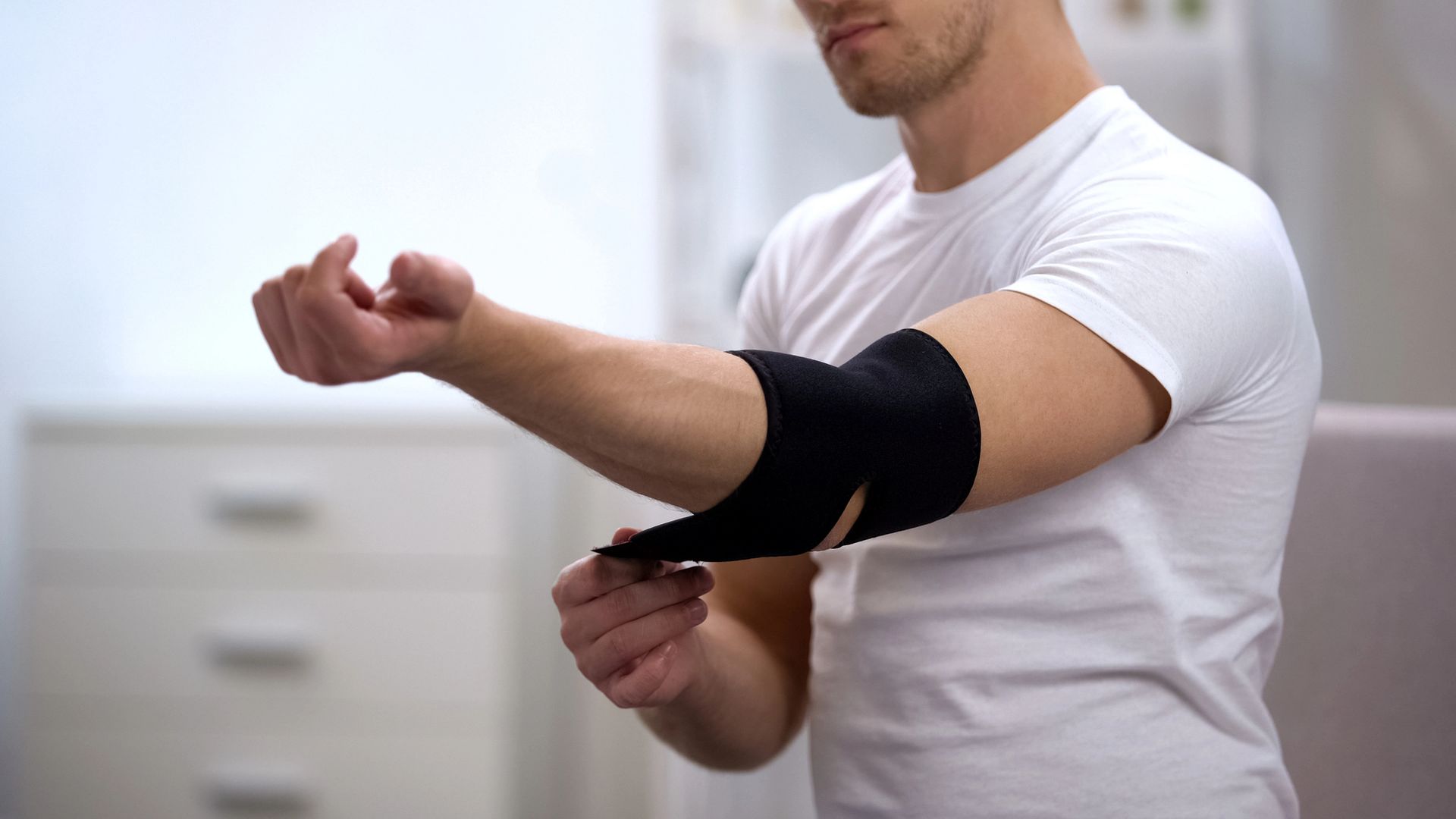 Persona que se coloca una codera negra en un brazo doblado mientras lleva una camisa blanca.
