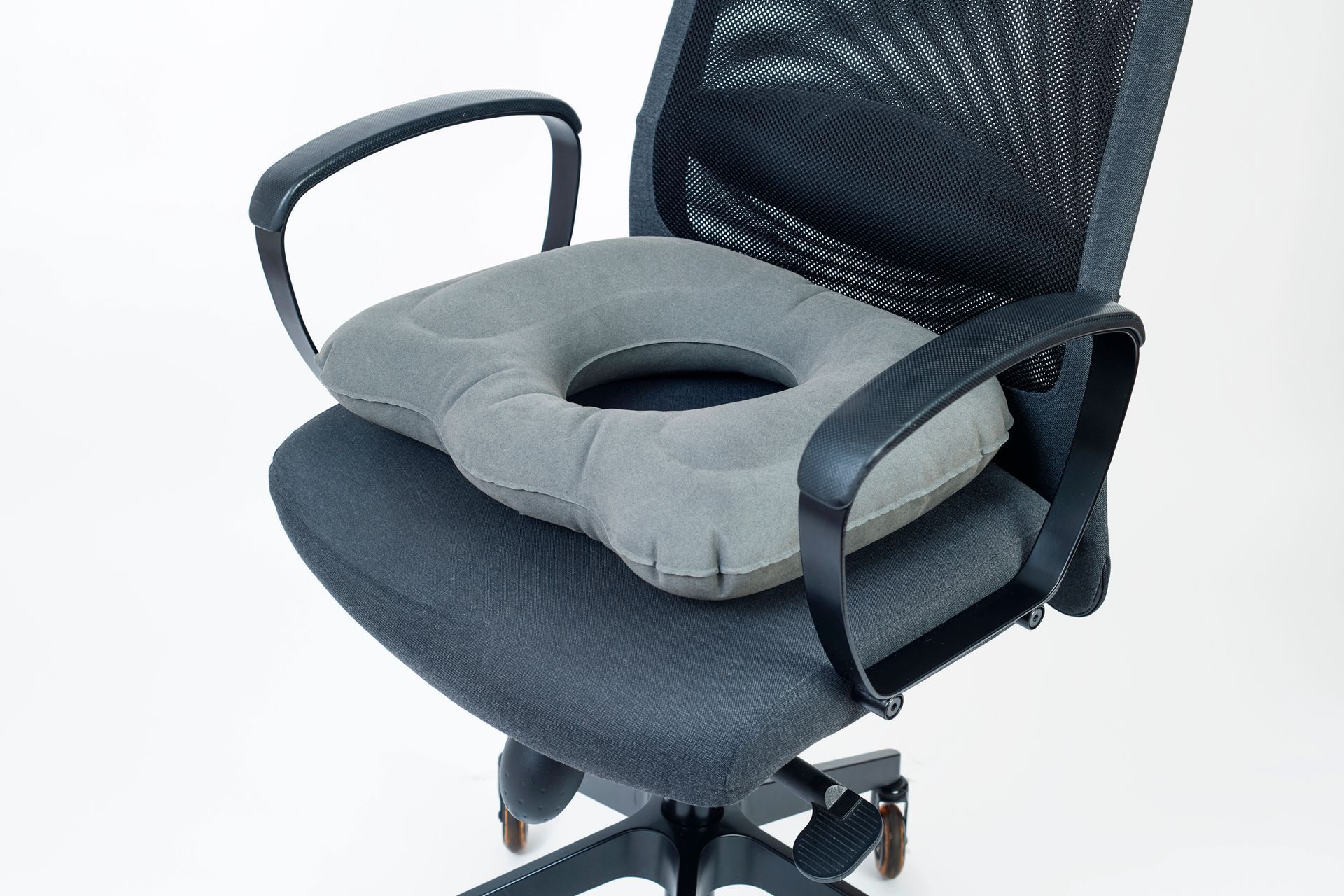 Silla de oficina con cojín de asiento gris en forma de U y orificio central, reposabrazos negros y respaldo de malla.