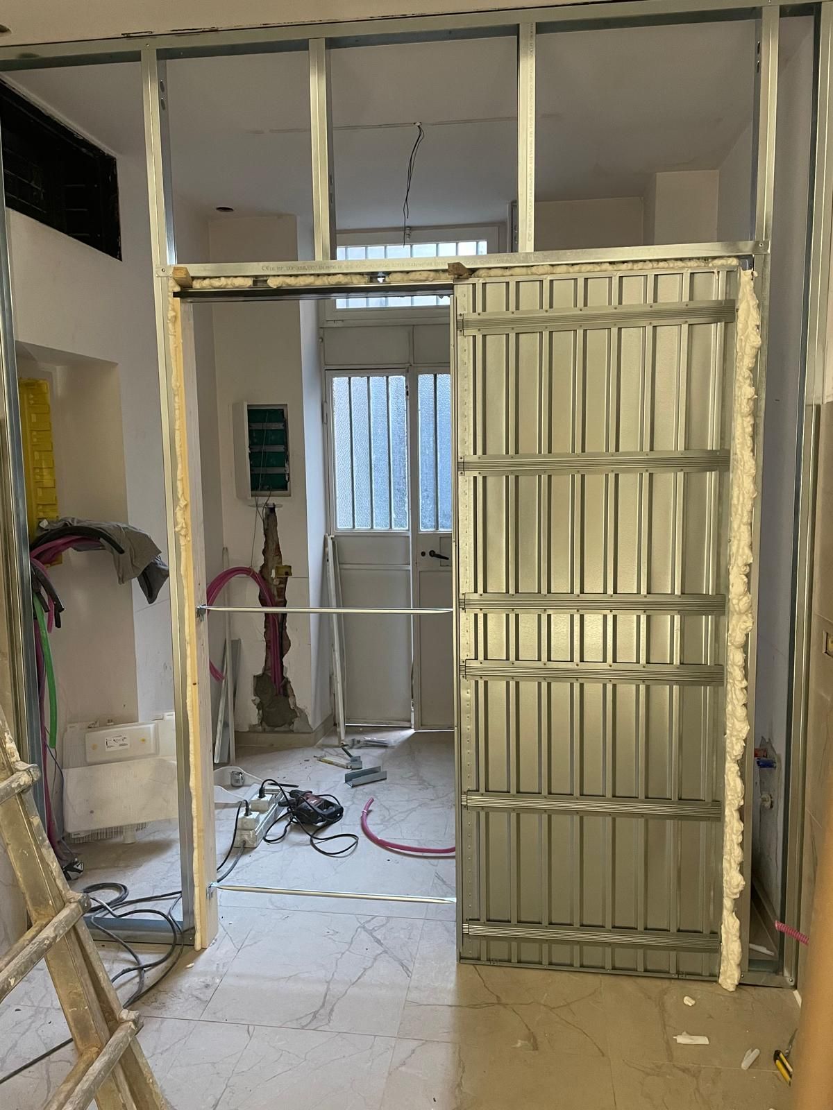 Interno in fase di ristrutturazione con struttura a vista, cancello in metallo e attrezzi da cantiere sul pavimento.