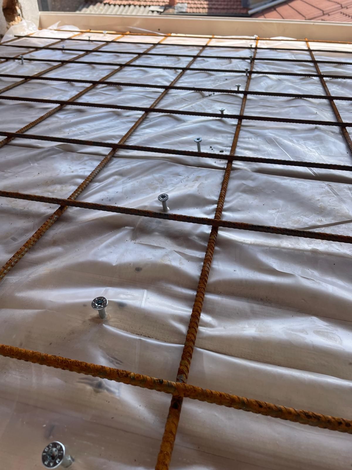 Rete metallica di rinforzo su un telo di plastica bianca in un cantiere edile, vista dall'alto.