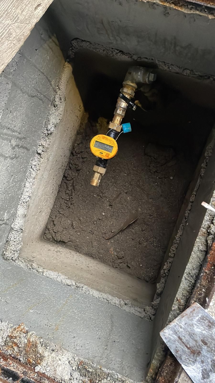 Pozzetto di servizio aperto con valvola del gas gialla e tubazioni collegate all'interno di un involucro di cemento.