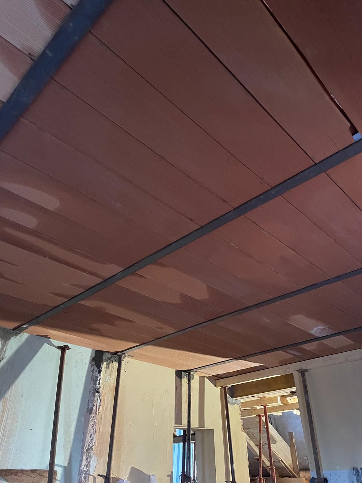 Soffitto interno in fase di costruzione con pannelli rossi e travi di sostegno scure.