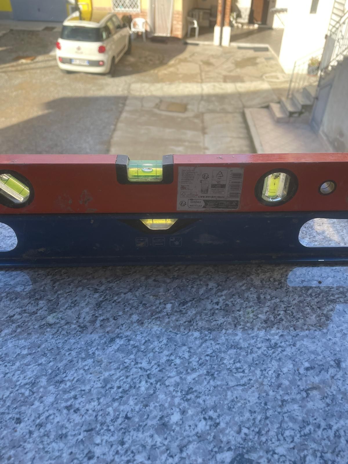 Livella a bolla su una superficie scura, con un cortile e un'auto parcheggiata sullo sfondo.
