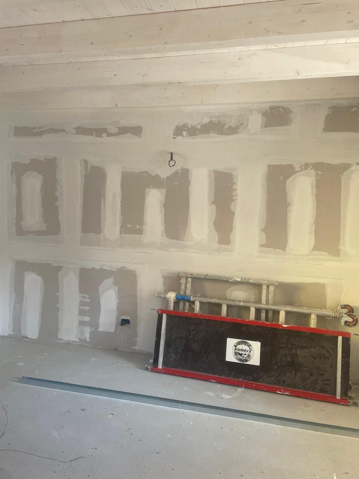 Interno di una stanza in fase di ristrutturazione con pareti in cartongesso non rifinite, faretti a incasso sul soffitto e un lungo camino incorniciato da nastro adesivo rosso.