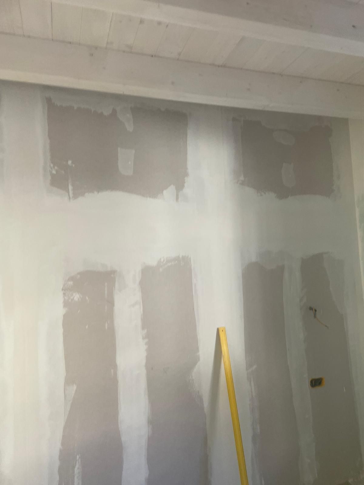 Parete interna parzialmente intonacata con stucco grigio e livella gialla appoggiata ad essa.