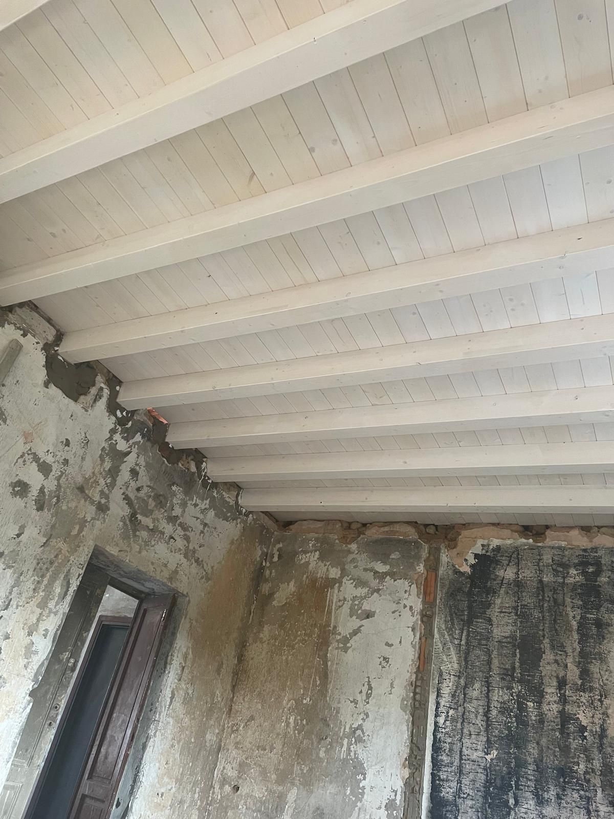 Angolo di stanza ammuffito e danneggiato dall'acqua, con pareti scrostate e soffitto rivestito di pannelli bianchi.