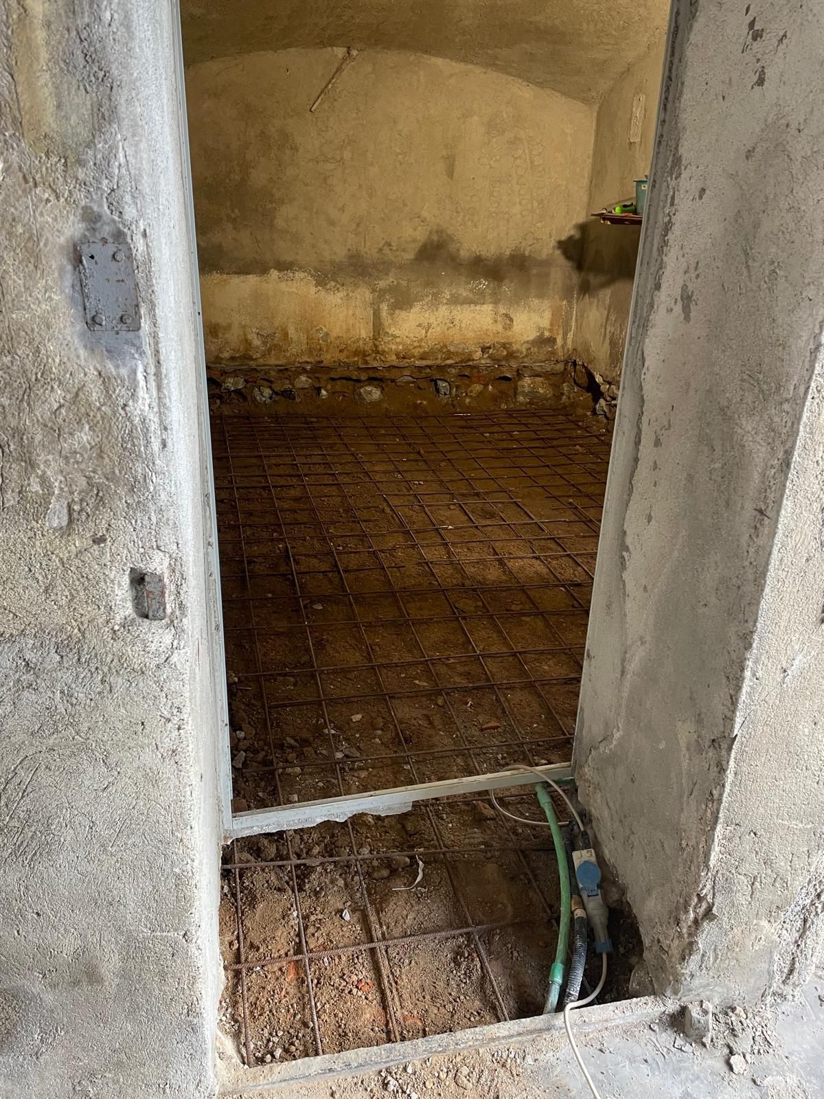 Si apre una porta su una piccola stanza non rifinita con pavimento in mattoni a vista e pareti intonacate a vista.