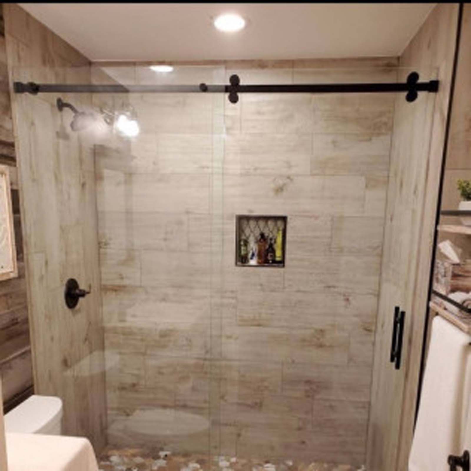 Shower with wood-look tile, glass door on a sliding track, and built-in niche. Black hardware, neutral colors.