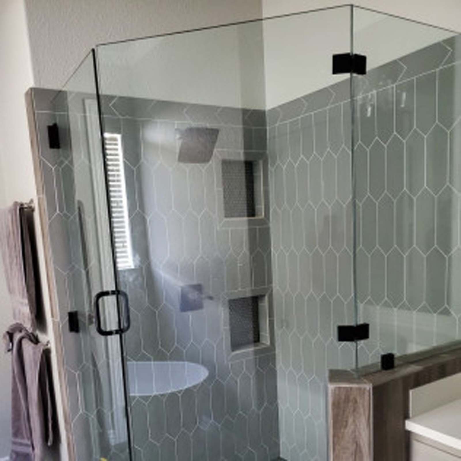 Glass shower enclosure with gray tile walls and black hardware.