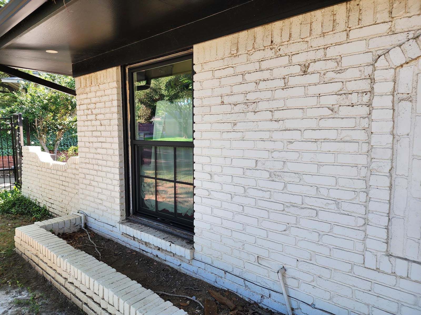 White brick exterior wall with a window and a black awning. A small, built-in planter is visible.