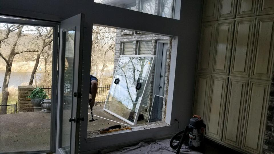 Interior view of a house during window replacement, with view of trees and water outside.