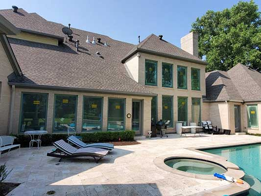 Backyard with pool, patio, and house. Loungers face the pool, sunlight reflects off windows.