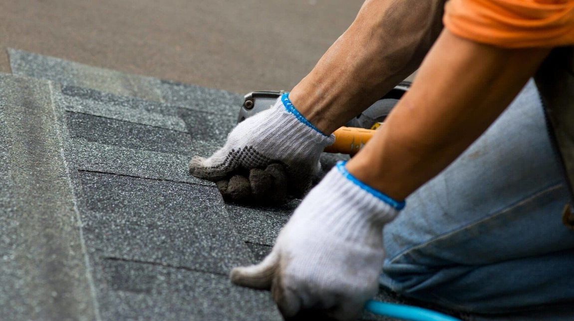 A man wearing gloves is working on a roof.