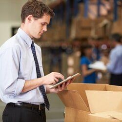 A man is looking at a tablet in a warehouse.
