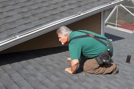 A man in a green shirt is kneeling on a roof.