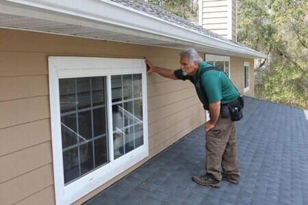 A man is looking at a window on the side of a house.