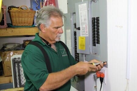 A man in a green shirt is working on an electrical box.