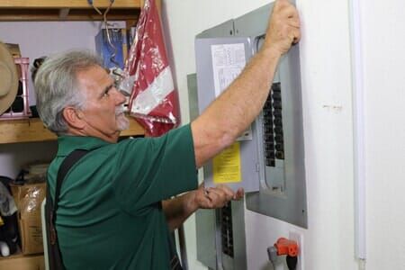 A man in a green shirt is working on an electrical box on a wall.